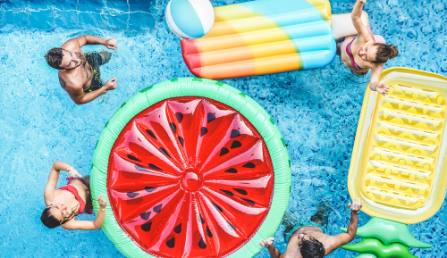 group of people in a swimming pool with rafts shaped like fruit